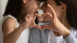 Close up of young woman and cute little daughter make heart sign with hands